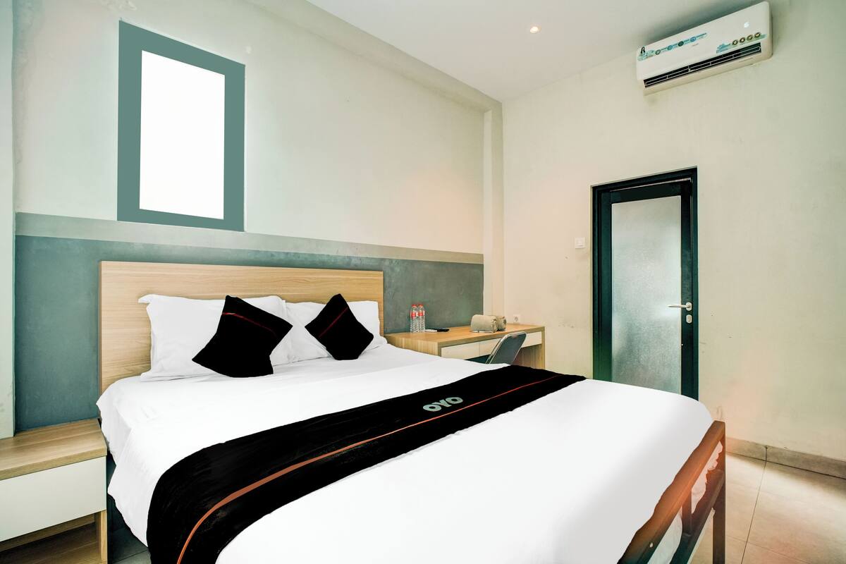 A hotel room with a bed, a desk, an air conditioner, and a door.