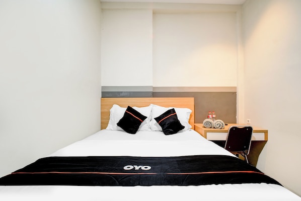 A neatly made bed with a black and white bedspread, two black pillows, and a wooden headboard. A small table with a chair and a bottle of water is visible to the right.