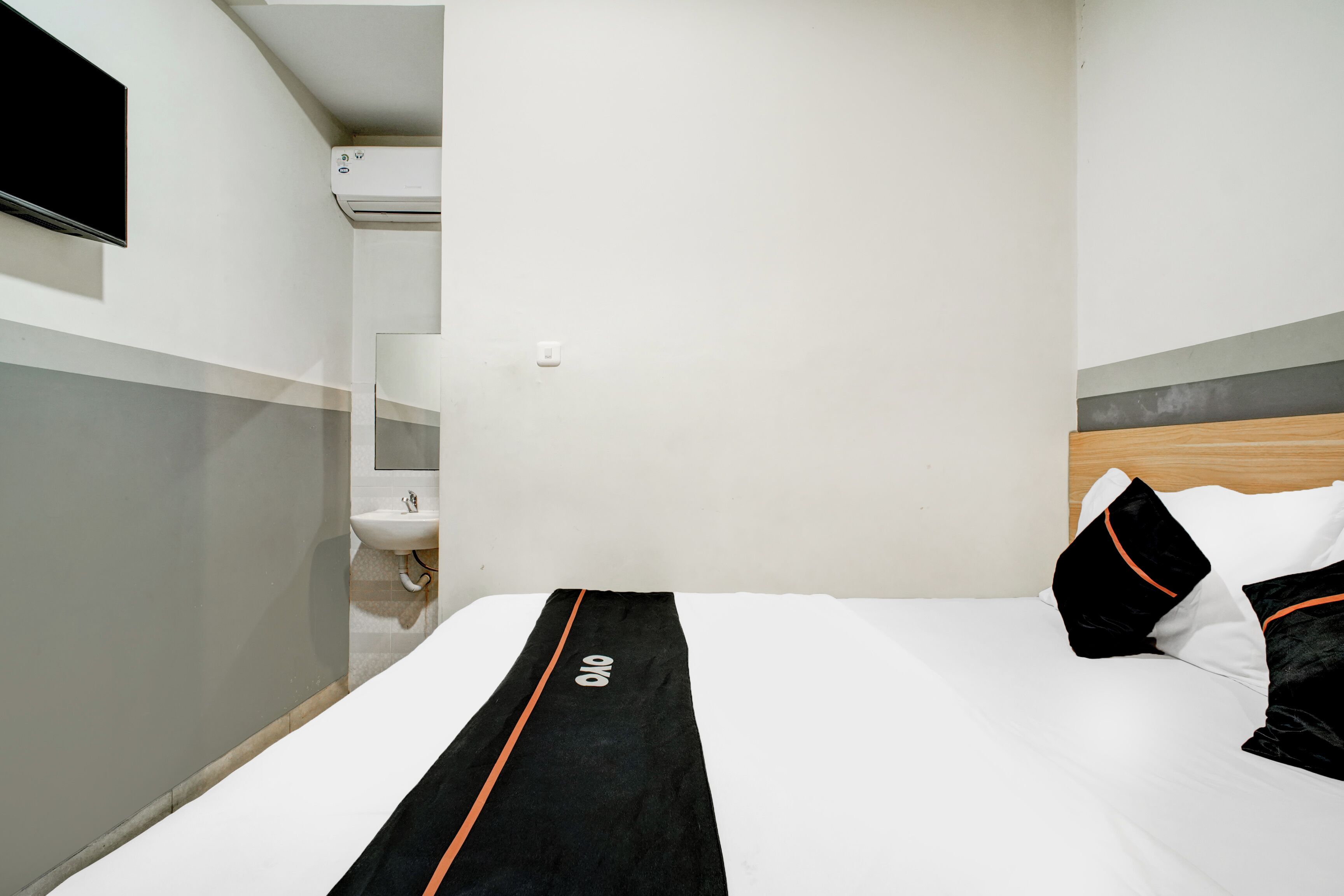 Una habitación de hotel con una cama, un televisor montado en la pared, un lavamanos y un equipo de aire acondicionado.