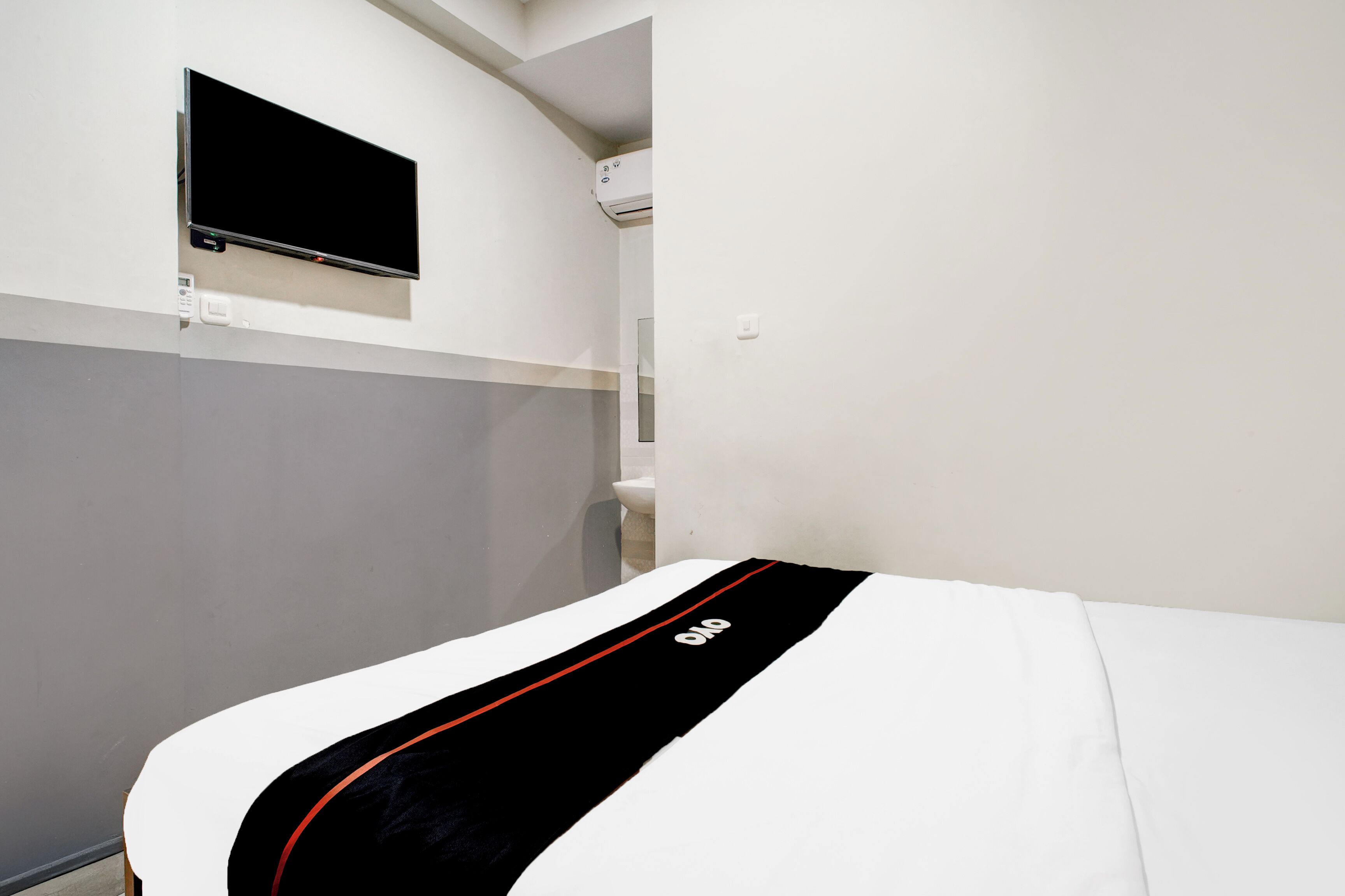 Una habitación de hotel con una cama, un televisor montado y un equipo de aire acondicionado.