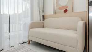 A beige sofa in a room with a white floor, a wooden headboard, and a framed abstract artwork on the wall. - 1BR with Infinity Pool Gym Rooftop C190 (Kamala)