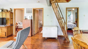 A spacious living area with a wooden staircase, a dining table, and a television in a wooden cabinet.