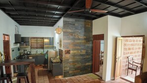 A spacious living area with a kitchen, a stone accent wall, and a ceiling fan.