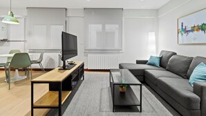 A modern living room with a sofa, a coffee table, a TV, and a dining area with chairs and a table.