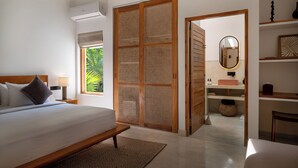 A bedroom with a bed, bedside table, and a large window. There is a wooden door with a woven screen, a mirror, and a shelf with decorative items. - SAMA Ahangama (Ahangama)