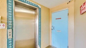A hotel room with a blue door, a tiled wall, and a metallic elevator. - Oceanfront Gem - Walk to Daytona Beach Pier! (Daytona Beach)