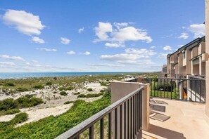 A balcony with a view of the beach and ocean, a building with a beige facade, and a clear sky.