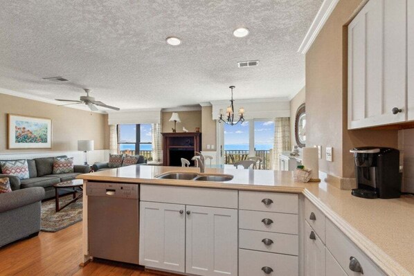 A modern kitchen with a central island, a dining area with a view, and a living room with a sofa and a painting. - 111 Sailmaker ~ Sea Time (Fernandina Beach)