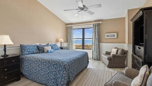Un dormitorio con cama, una silla, un mueble de televisión, un ventilador de techo y una ventana con vistas.