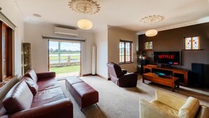 A living room with a large window, a sofa, a chair, a coffee table, and a TV displaying 'NETFLIX'. - Bunbury Bliss - Views and Vibes (East Bunbury)