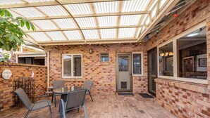 A covered patio with a brick wall, a table with chairs, and a glass door. - Bunbury Bliss - Views and Vibes (East Bunbury)