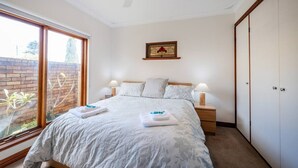 A bedroom with a bed, bedside lamps, a ceiling fan, a window with a view, and a wardrobe. - Bunbury Bliss - Views and Vibes (East Bunbury)