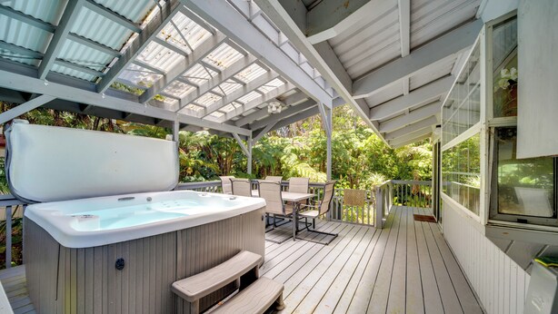 Une terrasse extérieure couverte, dotée d’un jacuzzi, d’un espace salon et offrant une vue sur une végétation luxuriante.