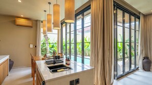 A modern kitchen with a central island, large windows, and a view of greenery.