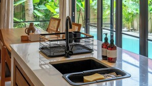 A modern kitchen with a large island, pendant lights, and a view of a tropical garden.
