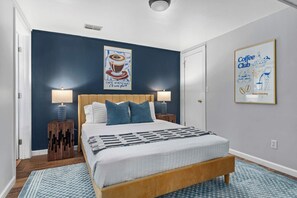 Une chambre à coucher avec un lit, deux lampes de chevet, une affiche sur le thème du café et une porte.