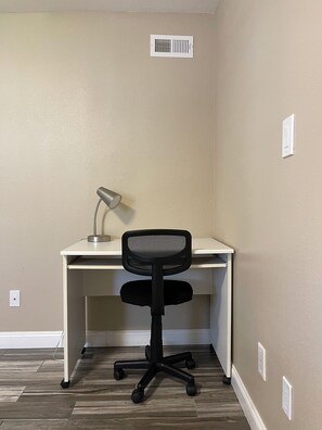 A corner office with a desk, chair, and a desk lamp.