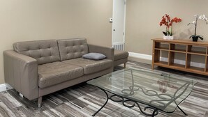 Ein modernes Wohnzimmer mit einem Ledersofa, einem Glastisch und einer Holztruhe mit zwei Topforchideen.
