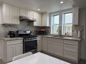 A kitchen with white cabinets, a stainless steel range, a microwave, and a window with a view. - Alameda Modern Victorian 2BD unit D (Alameda)