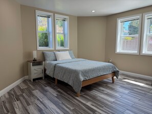 A bedroom with a bed, nightstand, and two windows. - Alameda Modern Victorian 2BD unit D (Alameda)