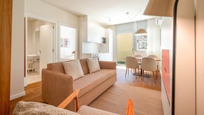 A modern living room with a sofa, a dining table with chairs, and a kitchen area in the background.