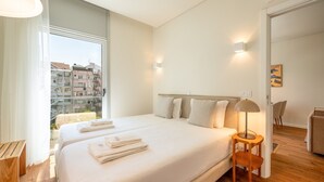 A modern hotel room with a large bed, two bedside tables, a lamp, and a view of the city through the window.