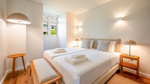 Une chambre moderne avec un grand lit, deux tables de chevet, un banc et une fenêtre donnant sur un beau paysage.