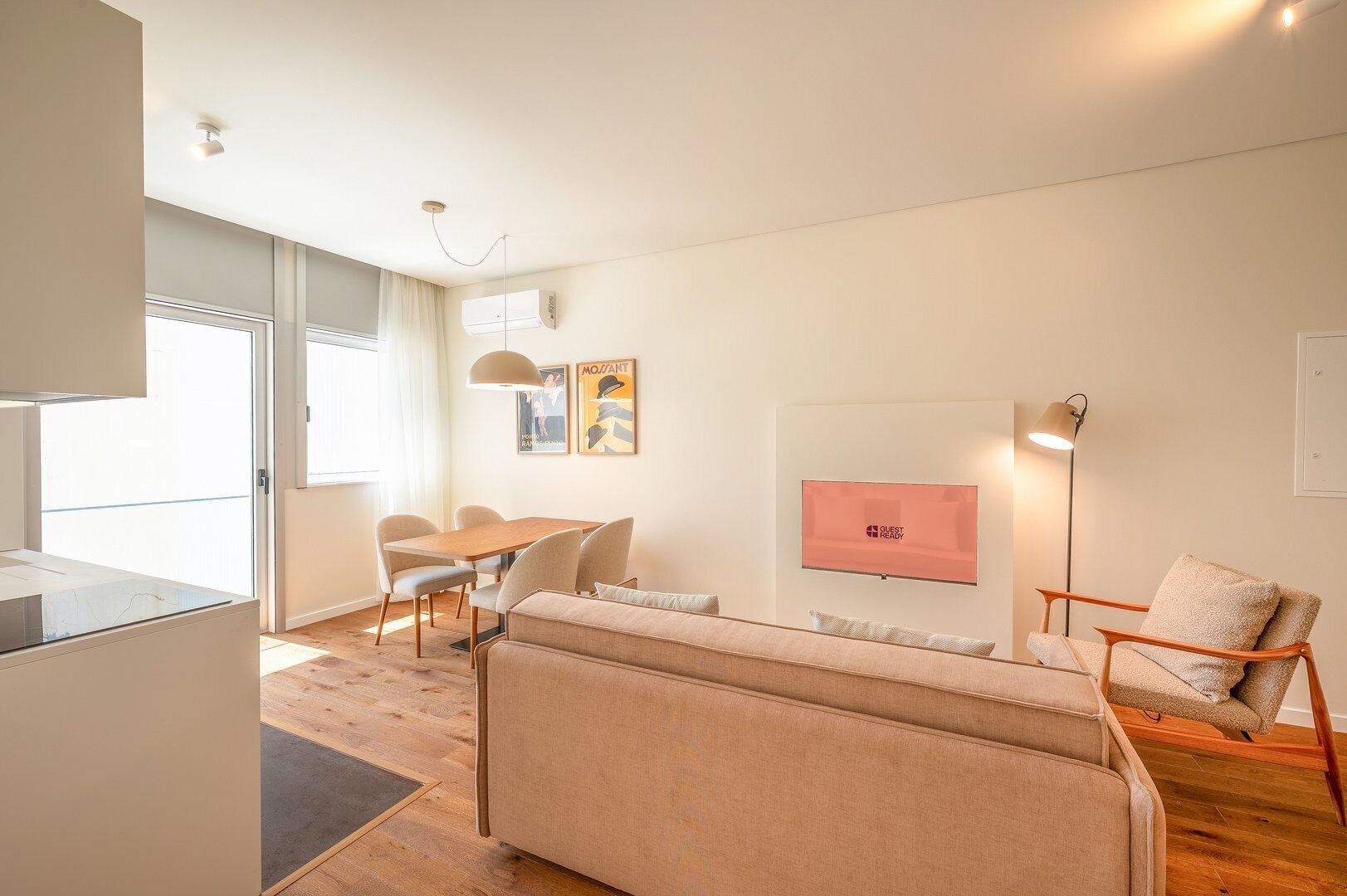 A modern living room with a sofa, dining table, chairs, a flat-screen TV, and a lamp.