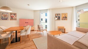 A modern living room with a wooden dining table, beige sofas, and a large window with a view of buildings.