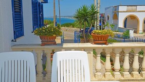 Een balkon met witte stoelen, planten in potten en uitzicht op zee.