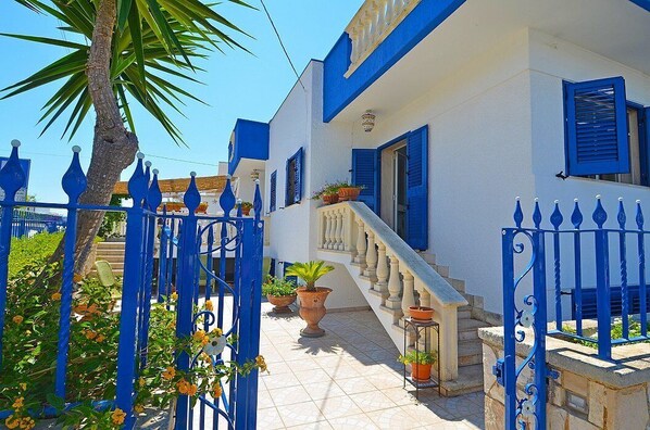 Un edificio blanco con contraventanas y una reja azules.