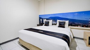 Ett hotellrum med en stor säng, ett nattduksbord och utsikt över en stadssiluett med berg i bakgrunden.