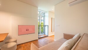 Una habitación moderna y luminosa, con suelo de madera, un sofá beige, una mesita pequeña y una pantalla rosa montada en la pared.