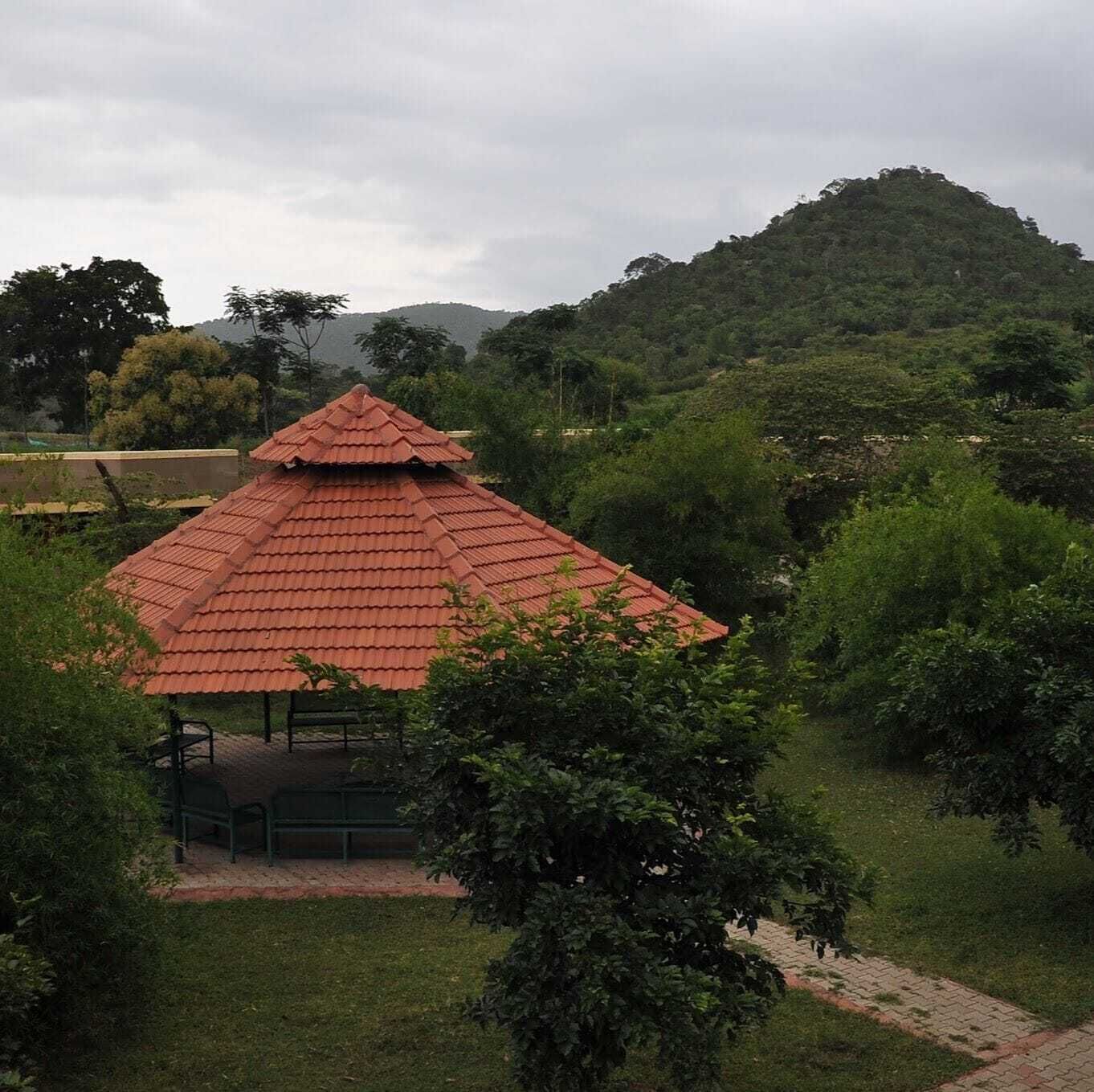 A gazebo with a red roof, surrounded by lush greenery and hills in the background.