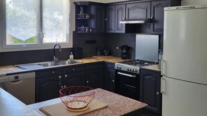 A modern kitchen with dark cabinetry, a gas stove, a refrigerator, and a window with frosted glass. - Family home in Fouras - enclosed garden near beach and market  (Fouras)