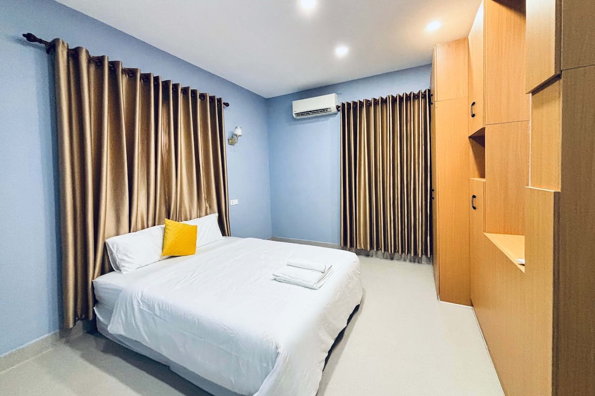 Una habitación de hotel con cama, cortinas, armario y equipo de aire acondicionado.