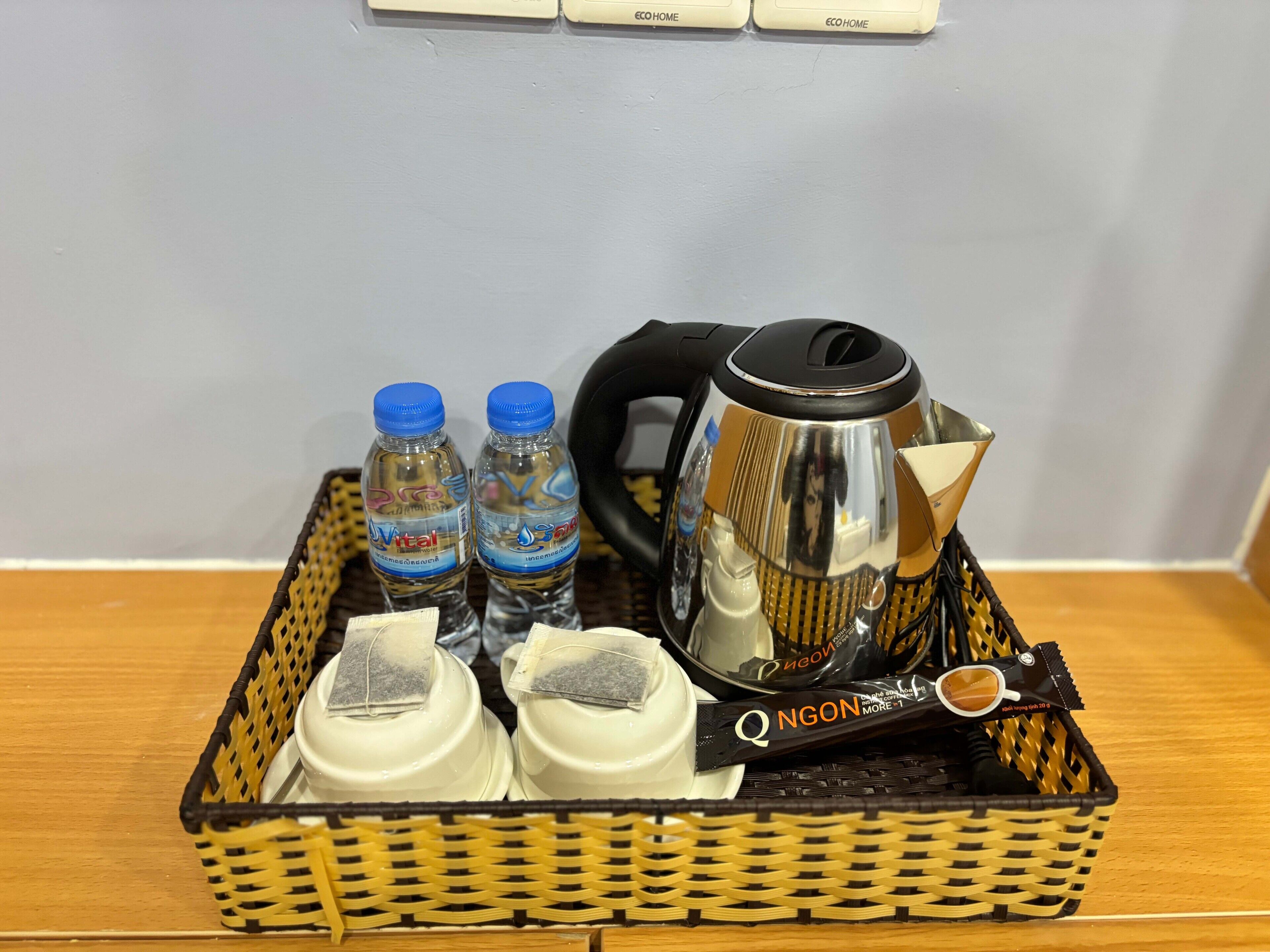 A wicker basket containing a kettle, two water bottles, a coffee pot, and a Q N G O N tea sachet.