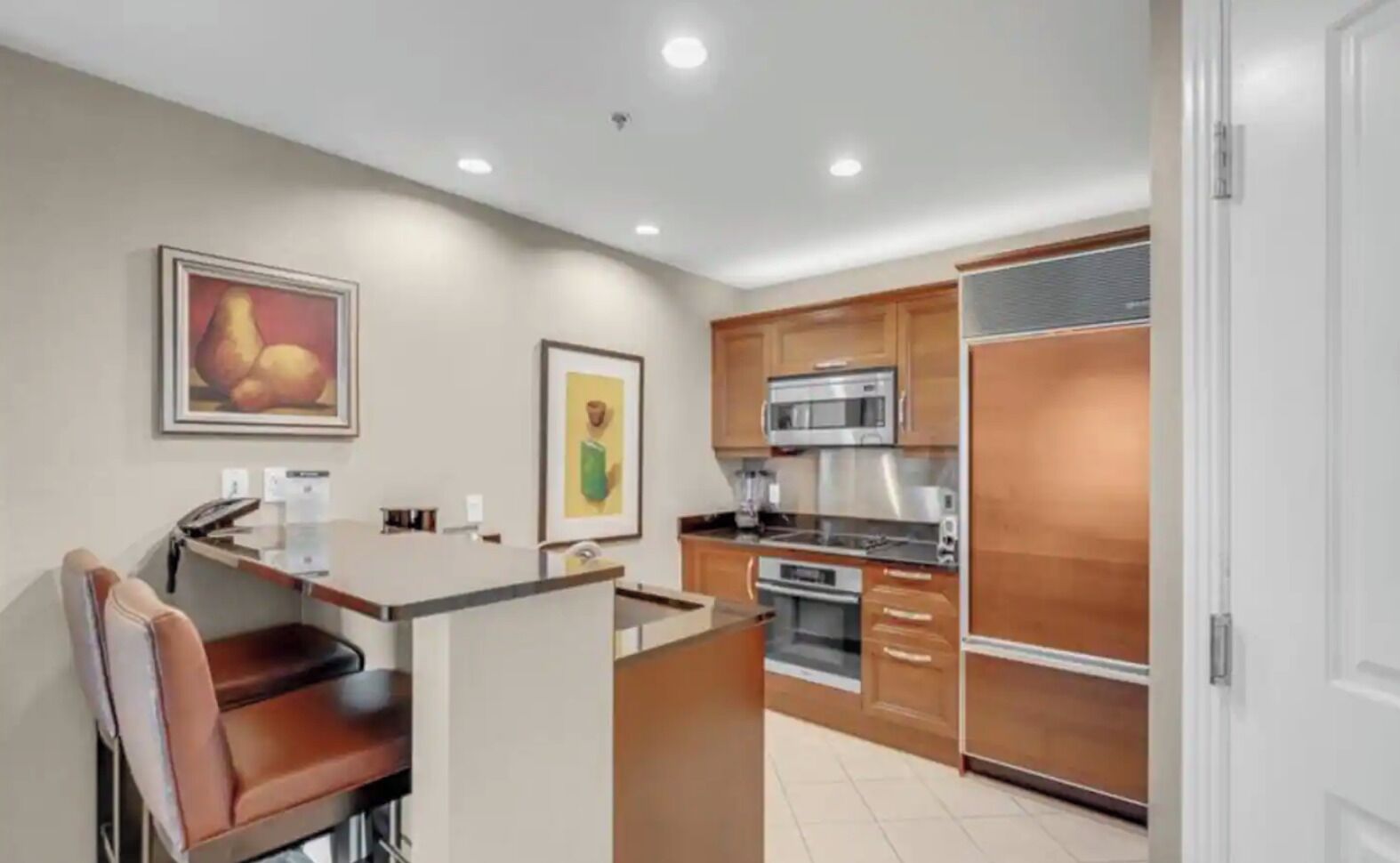 A modern kitchen with a central island, wooden cabinets, stainless steel appliances, and artwork on the walls.