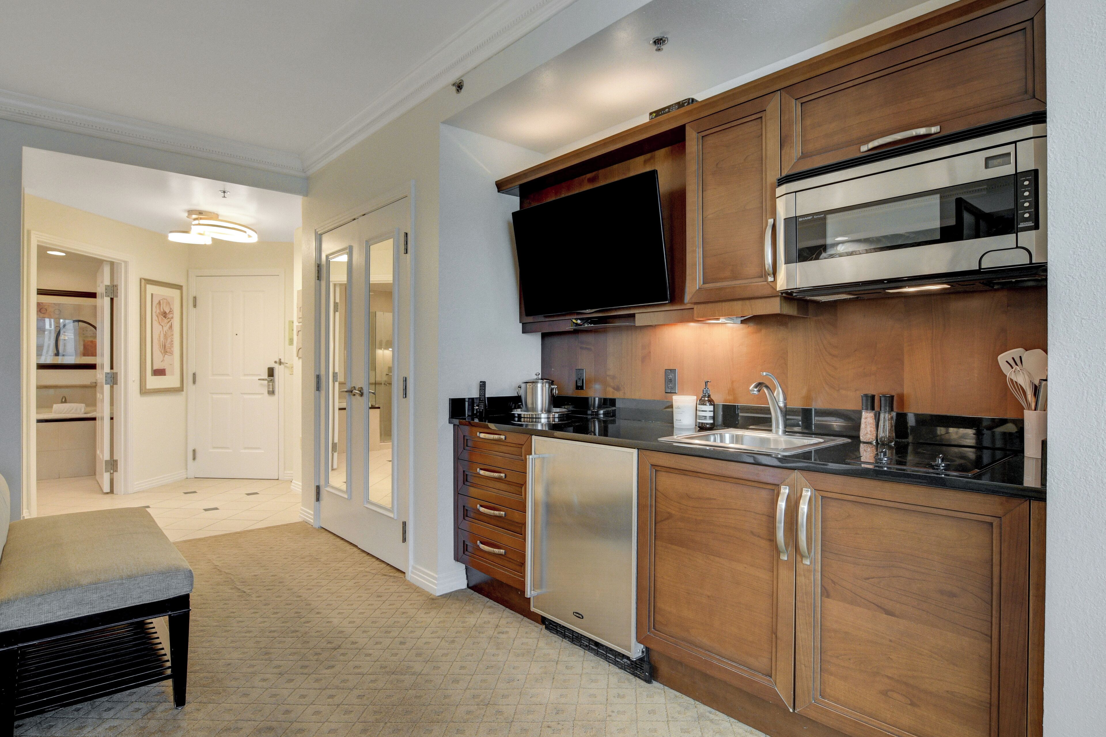 A modern kitchen with wooden cabinets, a stainless steel refrigerator, a microwave, and a black countertop.
