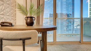 A modern room with a round wooden table, a potted plant, and a telephone. A large window offers a view of high-rise buildings. - Blu Cashmere Suite (Las Vegas)