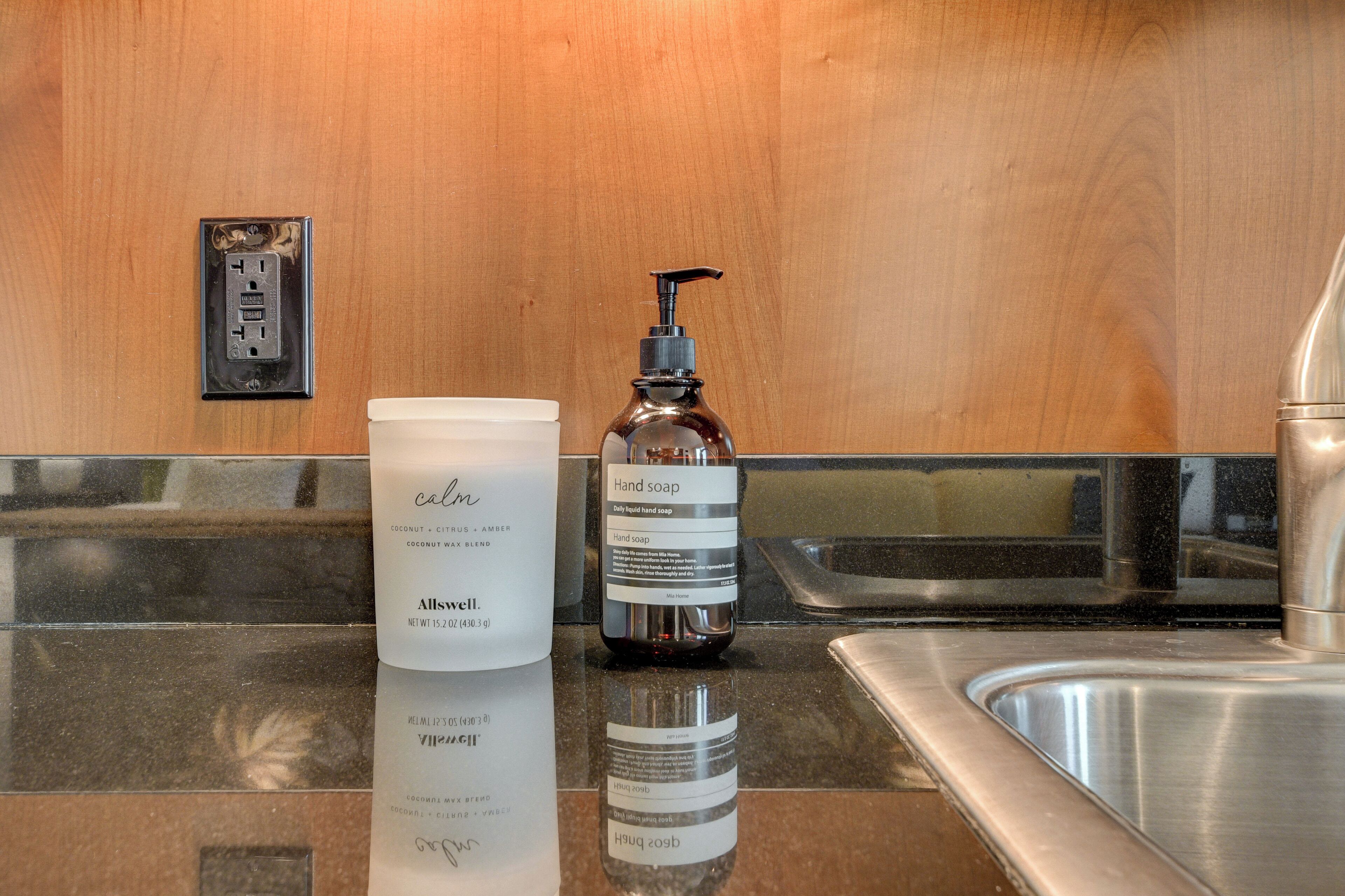 A bathroom counter with a hand soap dispenser and a bottle of liquid soap.