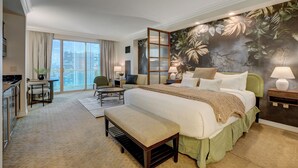 A spacious bedroom with a large bed, a seating area with a bench, a dining table, and a view of the city through large windows. - Blu Cashmere Suite (Las Vegas)
