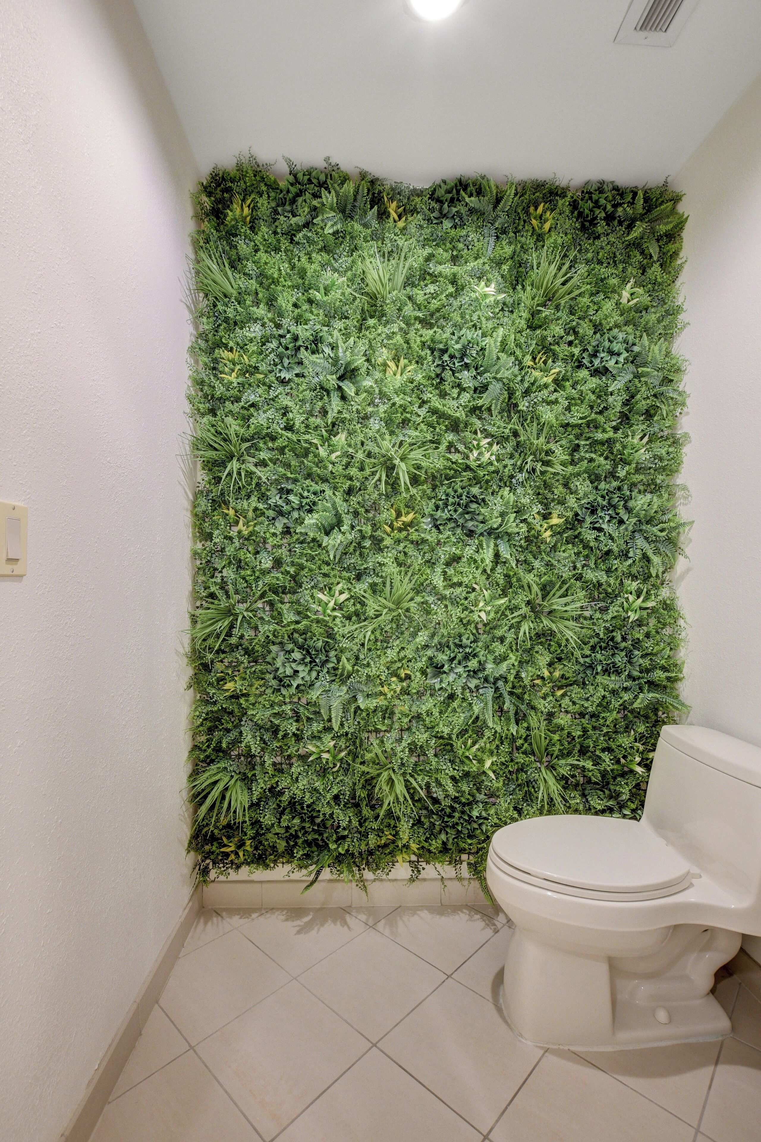 A bathroom with a green vertical garden wall, a toilet, and a light switch on the wall.