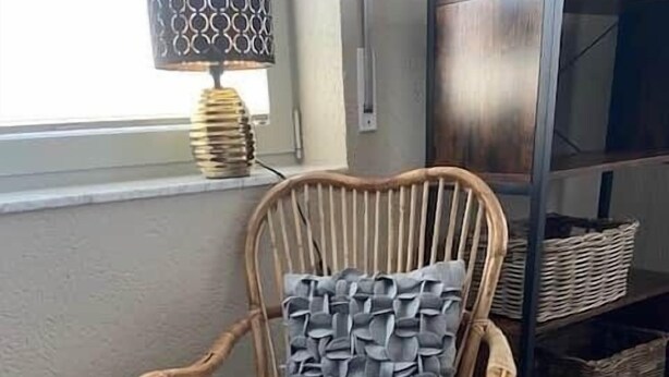 A wicker chair with a white cushion and a patterned pillow, placed on a wooden floor.