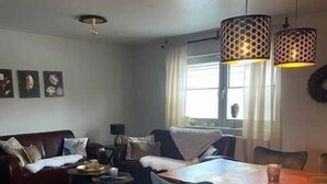 A living room with a sofa, a coffee table, and a dining table with chairs. There are two pendant lights above the dining table.
