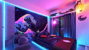 A bedroom with a bed, a chair, a wall tapestry, and a window with curtains. - Tokyo Shinjyuku Cyber Room (Tokyo)