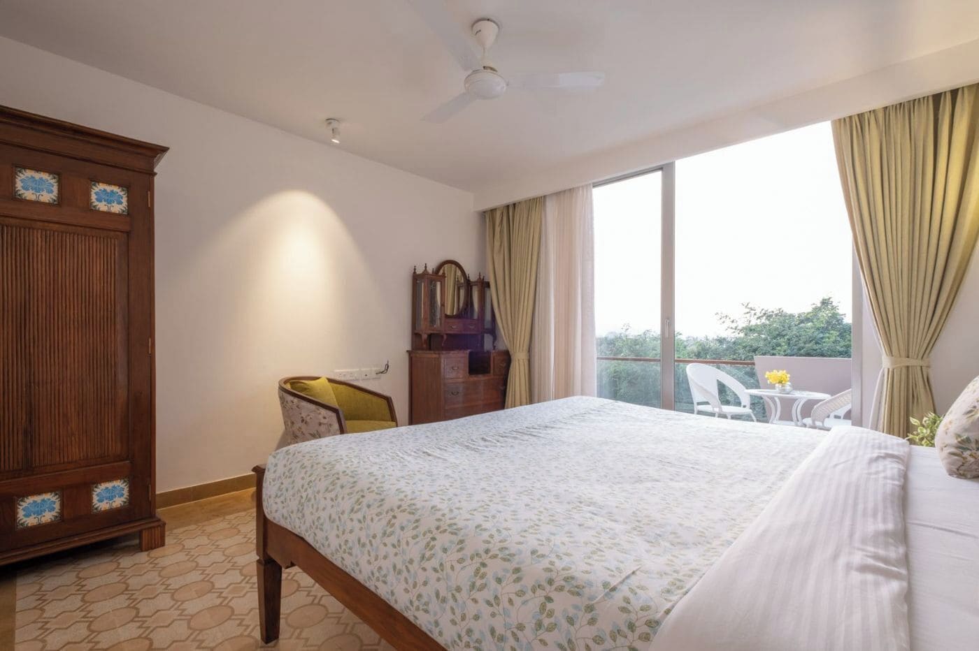 Una camera d'albergo con un letto, un armadio in legno, una sedia, una cassettiera e un balcone con tavolo e sedie.