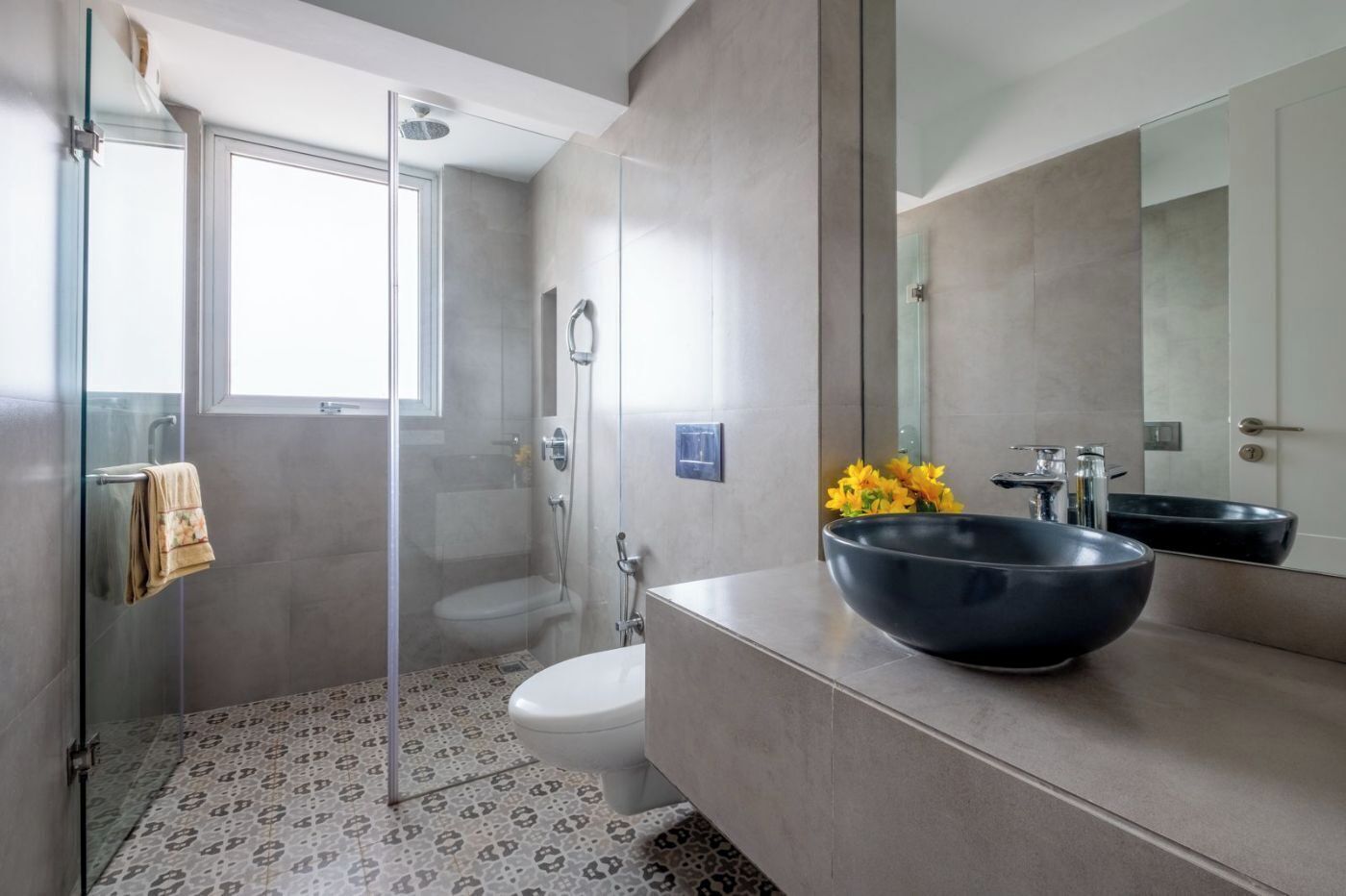 Ein modernes Badezimmer mit einer Duschkabine aus Glas, einer weißen Toilette, einem großen schwarzen Waschbecken und einem Spiegel, der den Raum wiederspiegelt.