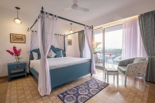 A bedroom with a four-poster bed, a nightstand, a chair, and a balcony with a table and chairs.