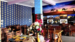 A restaurant with a high ceiling, patterned wallpaper, and a mural of a desert sunset. - Sunrise Hotel & Restaurant (Danta Ramgarh)